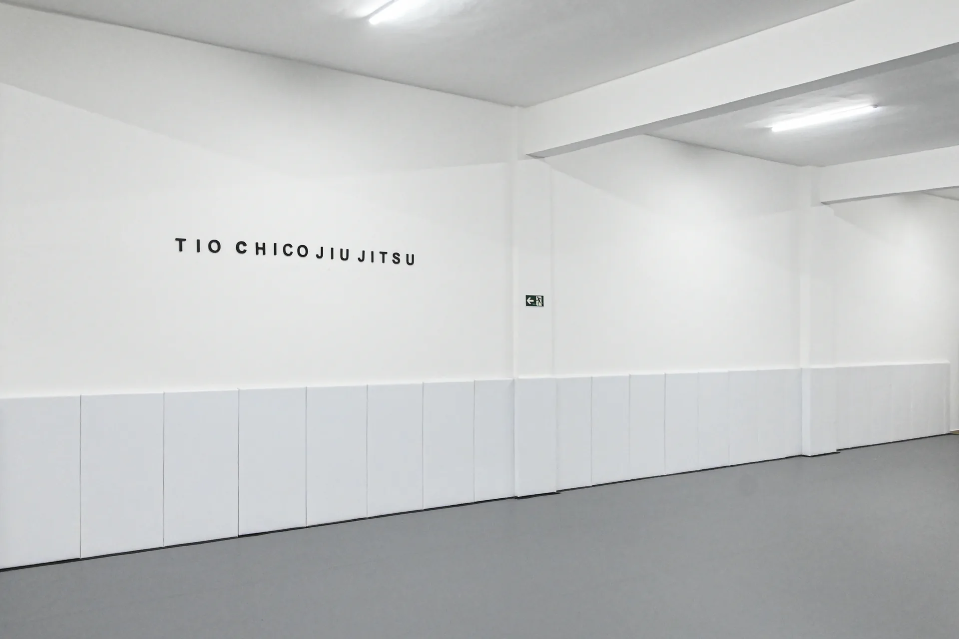 Parede branca com o letreiro Tio Chico Jiu-Jitsu no tatame